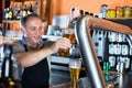 Barman is pouring unbottled beer with foam for client in the bar.