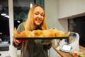 Smiling, glad, satisfied blond plump woman smell and present dough buns tray in the kitchen. Baking pastry on holidays