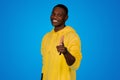 Smiling glad young black guy point fingers at camera, isolated on blue background, studio