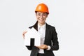 Smiling good-looking female asian saleswoman of construction company selling homes, wear helmet and business suit