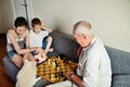 Smiling grandchildren with grandpa playing chess and looking at