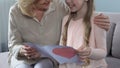 Smiling granddaughter gifting handmade greeting card with heart to grandmom