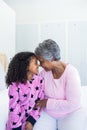 Smiling granddaughter and grandmother sitting face to face on bed Royalty Free Stock Photo