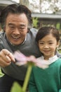 Smiling Grandfather and granddaughter looking at flower in garden