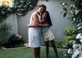 Smiling grandma and her granddaughter embrace while standing outdoors in the backyard