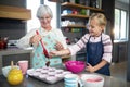 Smiling grandmother helping granddaughter while pouring cupcake batter