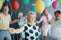 Smiling grandmother wearing a white blouse with black dots and holding colorful balloons during New Year`s Eve party with senior Royalty Free Stock Photo