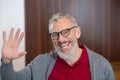 Smiling grey-haired bearded man waving his hand