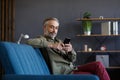 Smiling grey-haired man using mobile phone apps, texting message, browsing internet, shopping online. Looking at Royalty Free Stock Photo