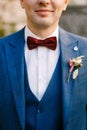 Smiling groom in blue plaid three-piece suit and white shirt with red bow-tie and boutonniere