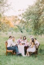 The smiling guests and newlyweds are celebrating the happy event in the sunny park, the wedding dinner.