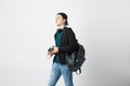 Smiling guy with a black backpack on his shoulder dressed in a dark green t-shirt, jeans, sweatshirt and a cap holds a Royalty Free Stock Photo