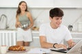 Happy young man using laptop in the kitchen while communicating with his girlfriend Royalty Free Stock Photo