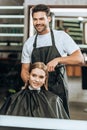 Smiling hairstylist using hair straightener and happy girl looking at mirror