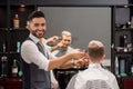 Smiling barber trimming client`s stylish haircut and looking at camera. Royalty Free Stock Photo