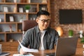 Smiling handsome adult asian male in glasses works with documents at workplace, has meeting in office interior Royalty Free Stock Photo