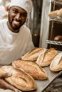 smiling handsome african american baker with tray of fresh loaves of bread