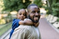 Smiling handsome African American father carrying his cute little daughter on back outdoors in city park. Daddy carrying Royalty Free Stock Photo