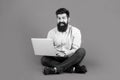 Smiling handsome bearded man worker laptop. Happy young man sitting on the floor with and using laptop computer on red Royalty Free Stock Photo