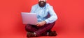 Smiling handsome bearded man worker laptop. Happy young man sitting on the floor with and using laptop computer on red Royalty Free Stock Photo