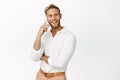 Smiling handsome blond man talking on mobile phone, calling on cellphone, standing over white background Royalty Free Stock Photo