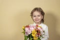 smiling handsome boy holds out a bouquet of colorful flowers on yellow background. happy child gives a bouquet of Royalty Free Stock Photo