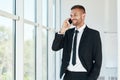 Smiling handsome businessman talking on phone in open space modern office with panoramic windows background Royalty Free Stock Photo