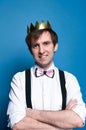 Smiling handsome man with dark hair in pink shirt with rolled up sleeves, bow tie, suspender and golden shiny homemade crown