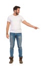 Smiling Handsome Man In Jeans And White T-shirt Is Standing And Pointing Down. Front View Royalty Free Stock Photo