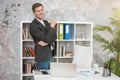 Smiling handsome man manager standing near his working place in office looking happy at the end of day. multitasking, work concept Royalty Free Stock Photo