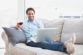 Smiling handsome man relaxing on sofa with glass of red wine using laptop Royalty Free Stock Photo