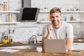 smiling handsome man working with laptop in kitchen and looking Royalty Free Stock Photo