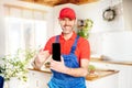 Smiling handsome plumber, repairman looking at camera in the kitchen, holding mobile phone and pointing at the empty screen.