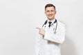 Smiling handsome young doctor man isolated on white background. Male doctor in medical gown, stethoscope pointing index Royalty Free Stock Photo