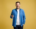 Smiling handsome young man browsing social media on mobile phone while standing on yellow background Royalty Free Stock Photo