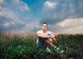 Smiling handsome young man sitting on on the green grass on a ba Royalty Free Stock Photo