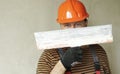 Smiling handyman repairman worker in overalls and protective orange helmet holds big putty knife for plastering concrete Royalty Free Stock Photo