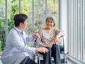 Smiling happy Asian elderly senior female patient sitting in wheelchair talking with friendly man doctor in white coat. Royalty Free Stock Photo