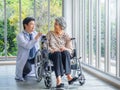 Smiling happy Asian elderly senior female patient sitting in wheelchair talking with friendly man doctor in white coat. Royalty Free Stock Photo