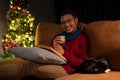 A smiling Asian man is relaxing on a couch with his cat in his living room on Christmas night Royalty Free Stock Photo