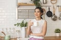 Smiling happy beautiful asian woman relaxing drinking cup of hot coffee or tea in kitchen at home Royalty Free Stock Photo