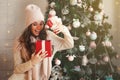 Smiling and happy, beautiful young woman in winter clothes with a red Christmas gift box on the background of a decorated Royalty Free Stock Photo