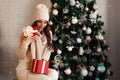 Smiling and happy, beautiful young woman in winter clothes with a red Christmas gift box on the background of a decorated Royalty Free Stock Photo