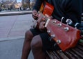 Black guy playing a guitar and singing happy sitting in a bench of a park