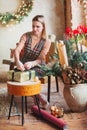 Happy blonde woman sitting on chair in new year festively packing christmas gift box