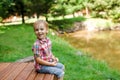 Smiling happy boy sitting on bench near lake. Summer time weekend mood. Royalty Free Stock Photo