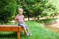 Smiling happy boy sitting on bench near lake. Summer time weekend mood. Royalty Free Stock Photo