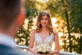 Smiling Happy Bride Holding Wedding Bouquet In Front Of Groom at Wedding Ceremony Outdoors At Park. Groom Is On Royalty Free Stock Photo