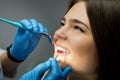 Smiling happy brunette woman patient examined by dentist in blue gloves using dental mirror and scaler sitting half a turn in