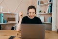 Smiling happy businesswoman in headphones sits at desk, looks at laptop screen, making notes, participating Royalty Free Stock Photo